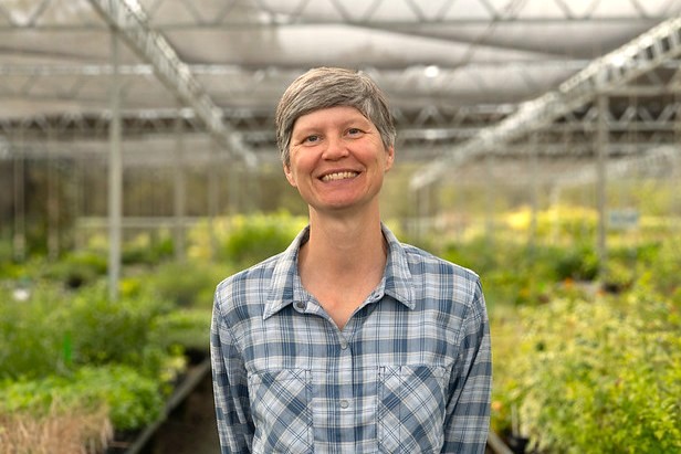 Smiling person with short hair in greenhouse wearing plaid shirt among potted plants (photo)