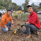 Program co-coordinators Chris Huang and Cameron Long take a break from planting a new plant to pose for a photo, kneeling with the landscape in the background.