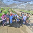 Image of a line of people standing in the foreground of a one-acre nursery filled to the brim with climate-appropriate plants; they are holding plants and smiling.