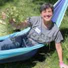 A person lays in a low hammock while showing off their weeding skills.